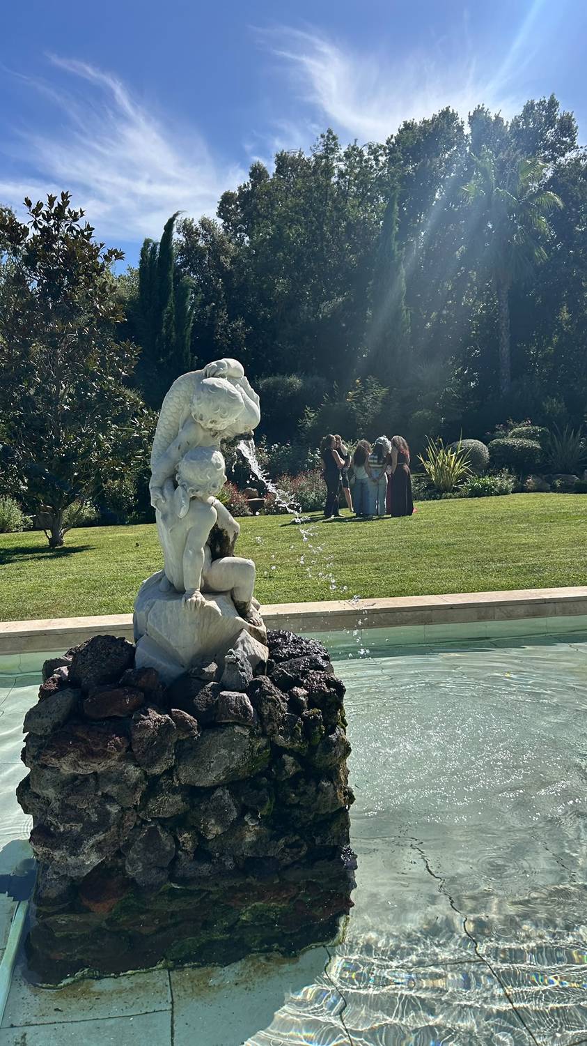 Fontaine ornée d'une statue dans les jardins à la française du château, avec un groupe de participants en discussion à l'arrière-plan
