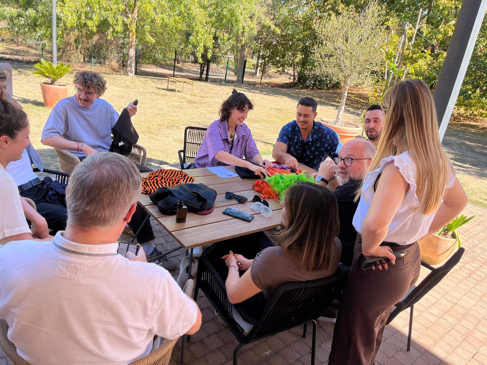Une équipe choisit et prépare ses costumes (rayures, plumes) en terrasse avant le tournage de sa séquence