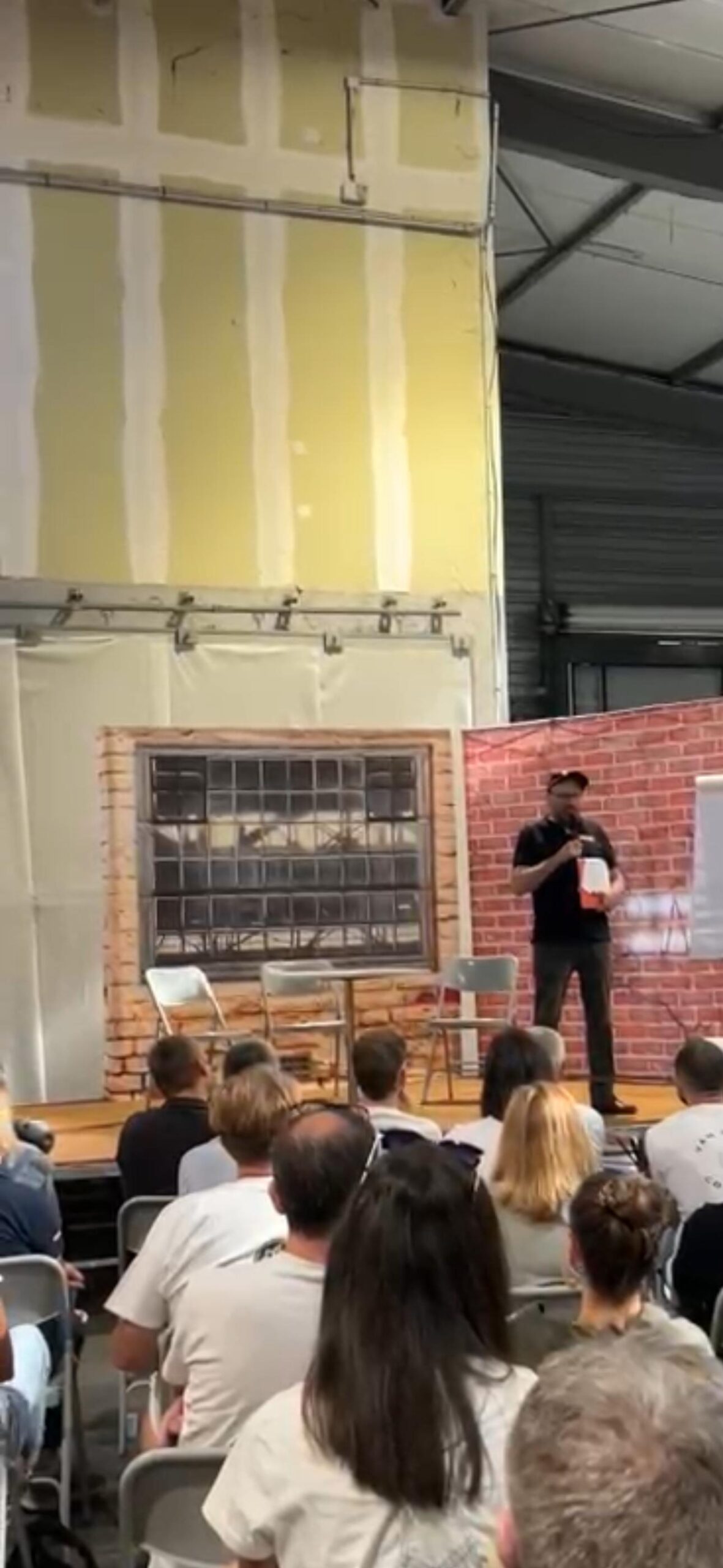Un comédien de MEEUS, micro et dossier en main, s'adresse directement au public depuis la scène du théâtre forum